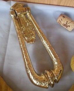Aldaba, llamador en hierro dorado. Forma de péndulo.